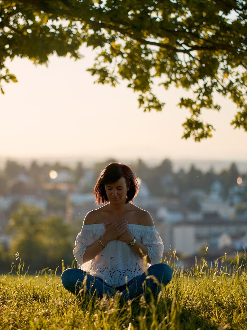 Nicole sitting in a meadow under a tree, hand on her heart, eyes closed